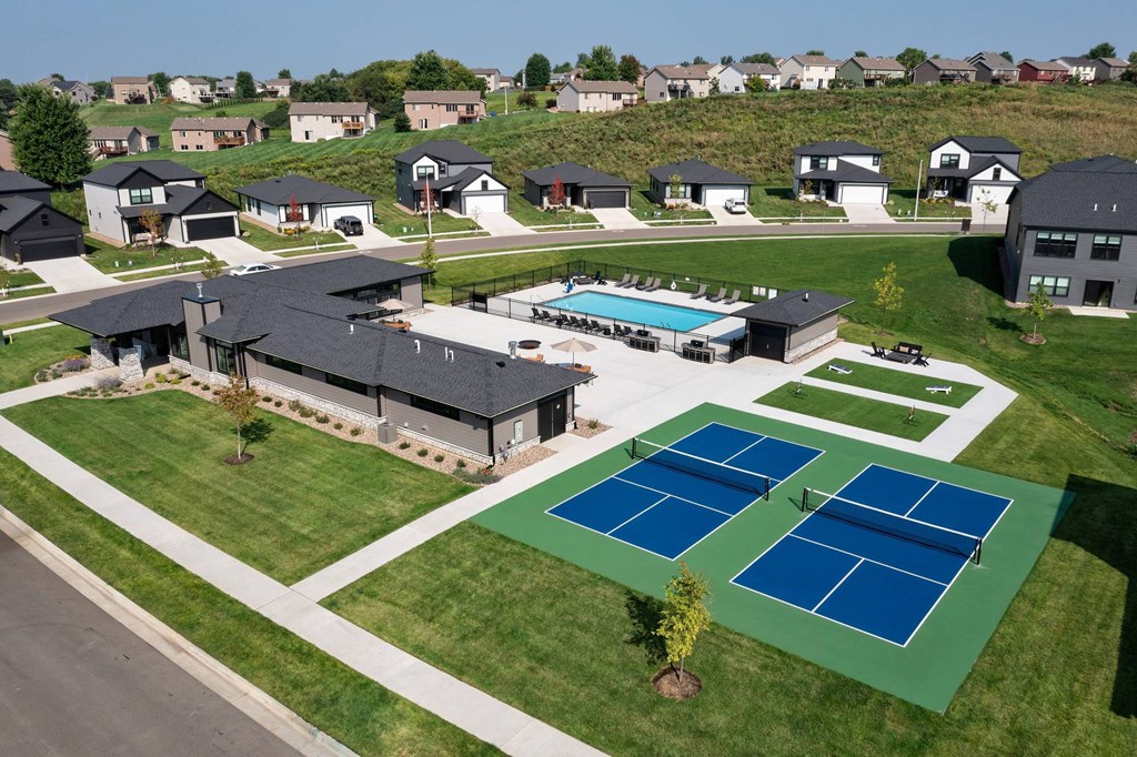 A tennis court is located in the foreground of a residential area.