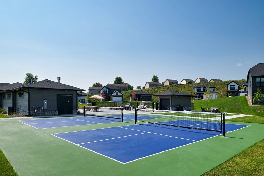 A tennis court with a green and blue surface is surrounded by houses.