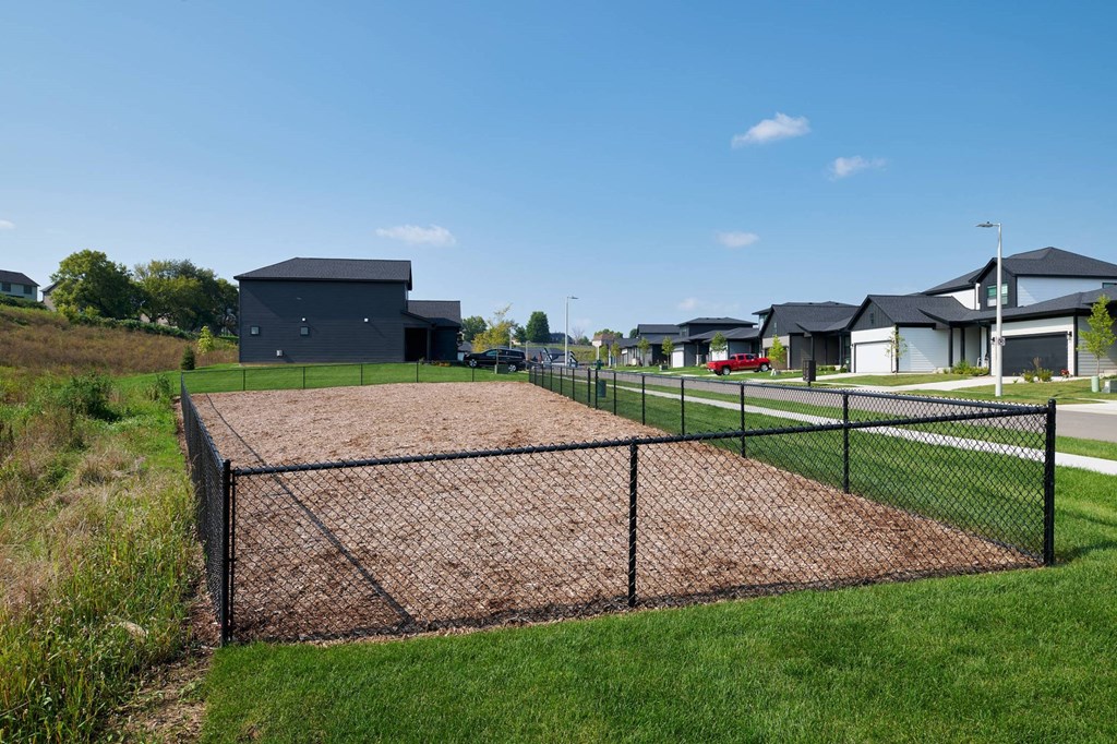 A dog park with a chain link fence and a building in the background.