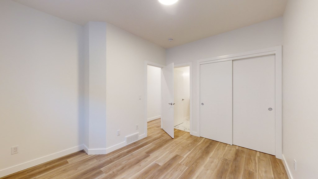 A room with white walls and wooden flooring with a door on the right.