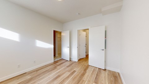 A room with white walls and wooden flooring with three doors.