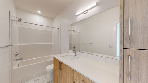 A white bathroom with a wooden vanity and a glass shower stall.