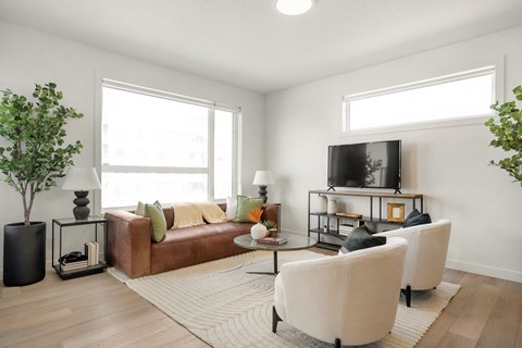 A living room with a brown couch, a white chair, and a television on a stand.