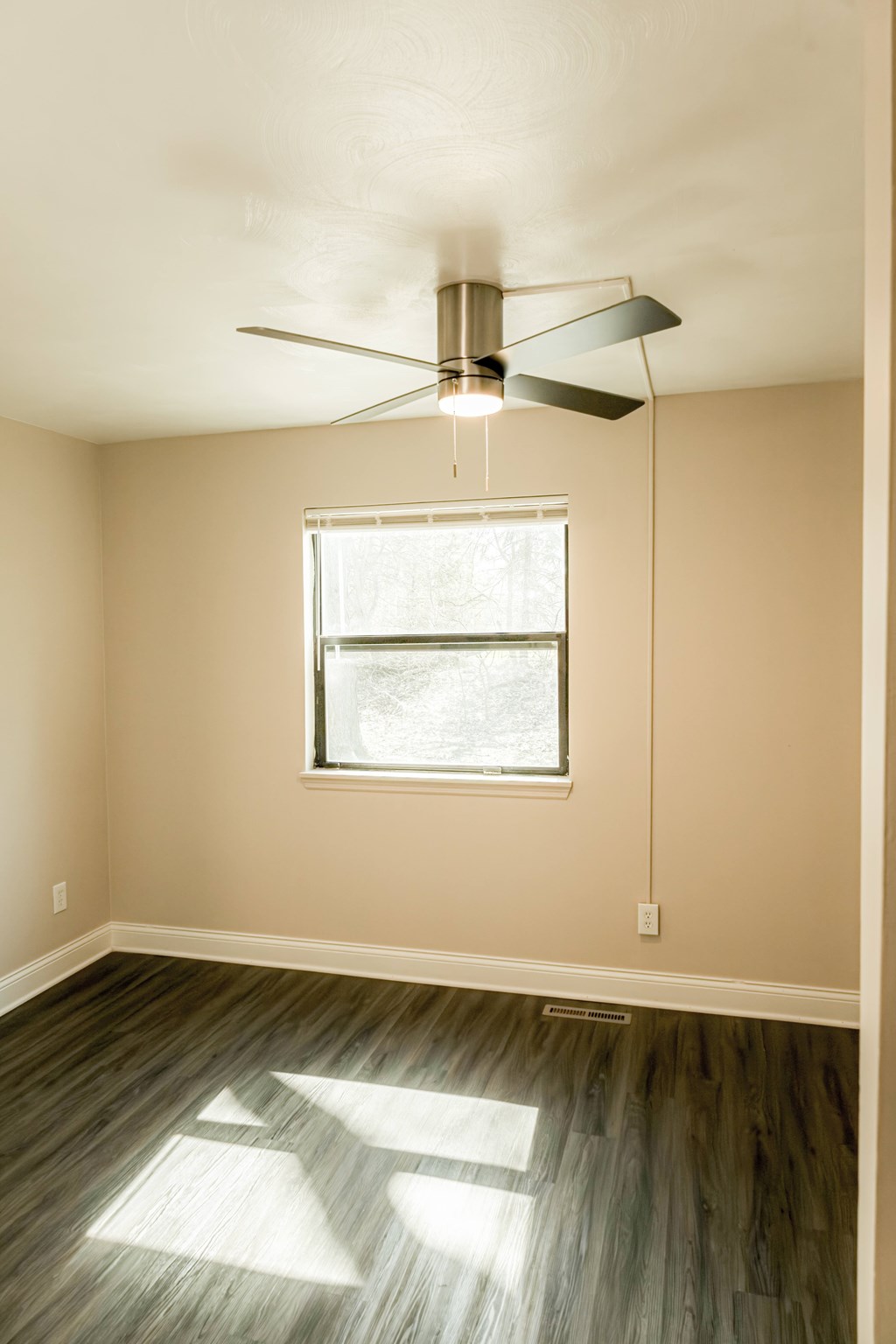 A room with a ceiling fan and a window letting in sunlight.