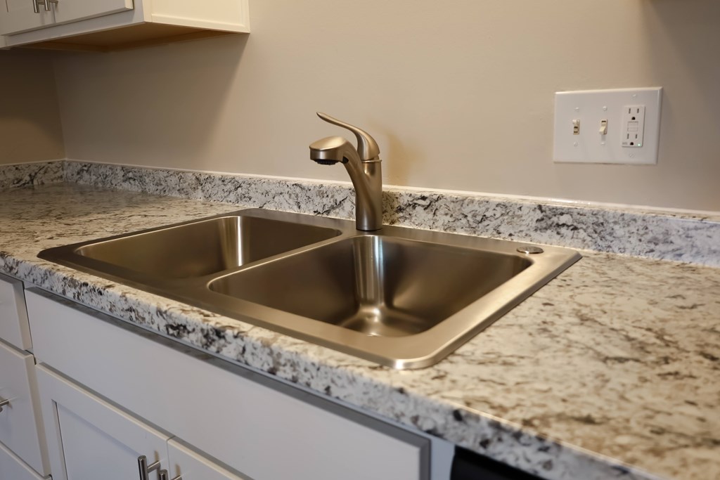 A kitchen sink with a faucet and a granite countertop.