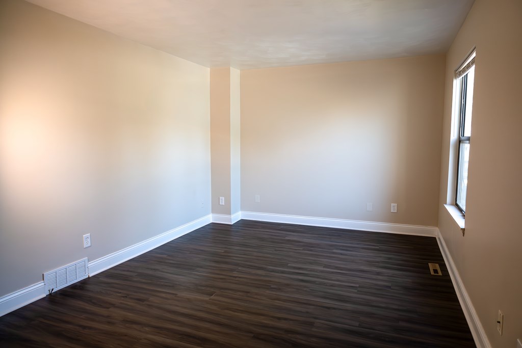 A room with wooden flooring and a window on the right side.