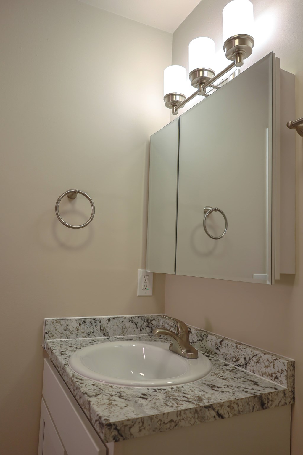 A bathroom with a marble counter top and a mirror with lights.