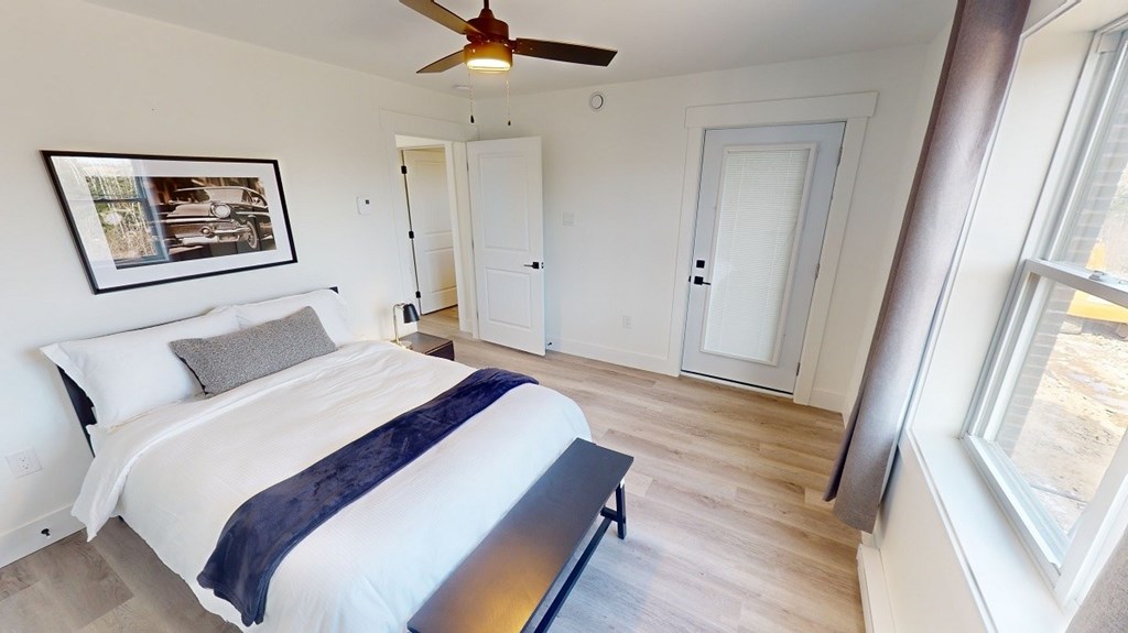 A bedroom with a bed, a ceiling fan, and a picture on the wall.