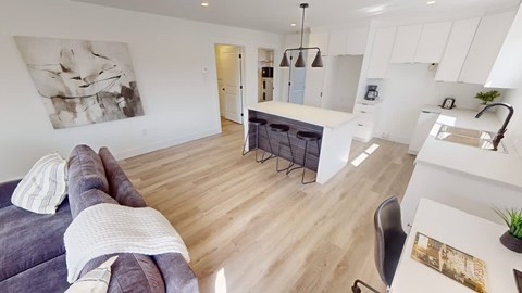 A modern living room with a grey couch and a white kitchen area.