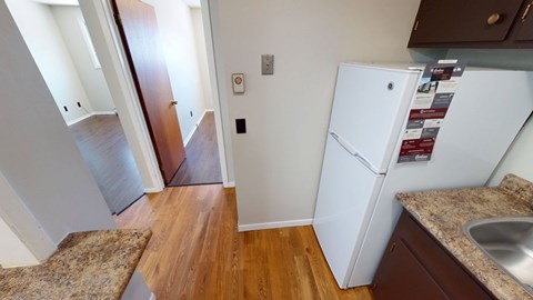 A kitchen with a white fridge and wooden floors.