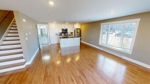 A spacious living room with wooden floors and a staircase on the left side.