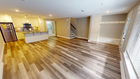 A spacious kitchen with wooden flooring and a refrigerator on the left.