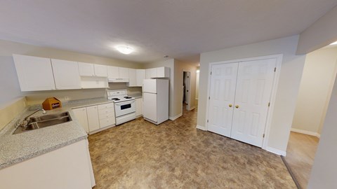 A kitchen with white cabinets and appliances, a sink, and a carpeted floor.