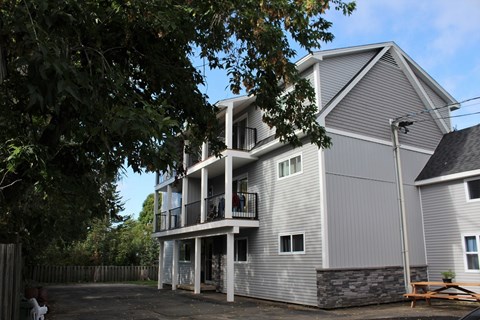 A grey house with a balcony and a tree in front.