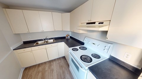 A white stove top oven with four burners is in a kitchen with white cabinets.
