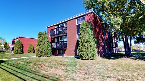 A red brick building with a balcony and trees in front.