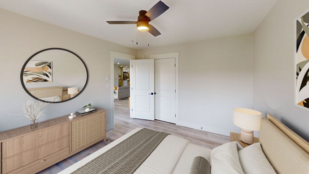 A living room with a brown rug, a white sofa, a wooden cabinet, a round mirror, and a ceiling fan.