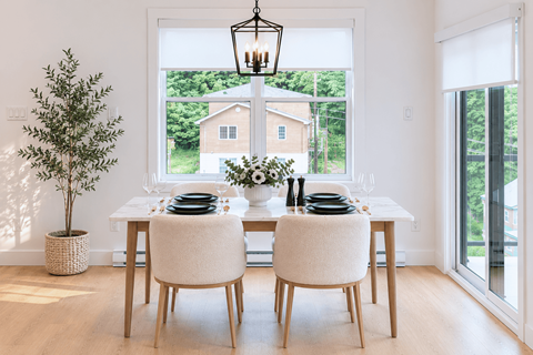 A dining room with a table set for two and a view of a house through the window.