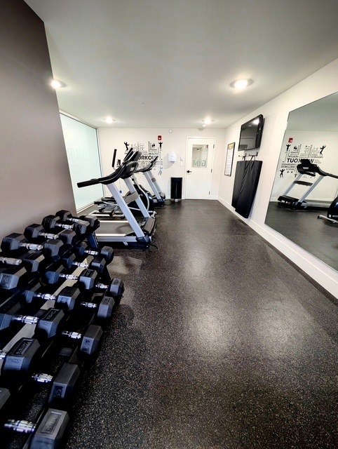A gym with a row of dumbbells on the left and a mirror on the right.