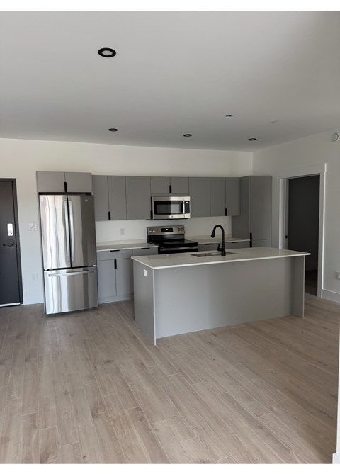 A modern kitchen with stainless steel appliances and wooden flooring.