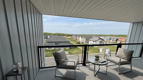 A balcony with two chairs and a table overlooking a residential area.