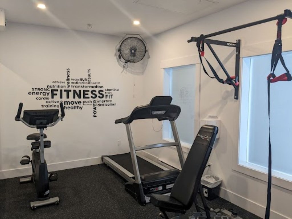 A gym room with a treadmill, exercise bike, and a wall with a fitness word cloud.