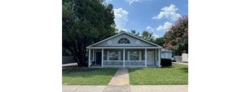 A small house with a porch and a tree in front.