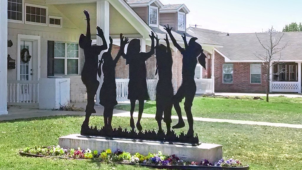 A statue of four people dancing is in the foreground of a residential area.