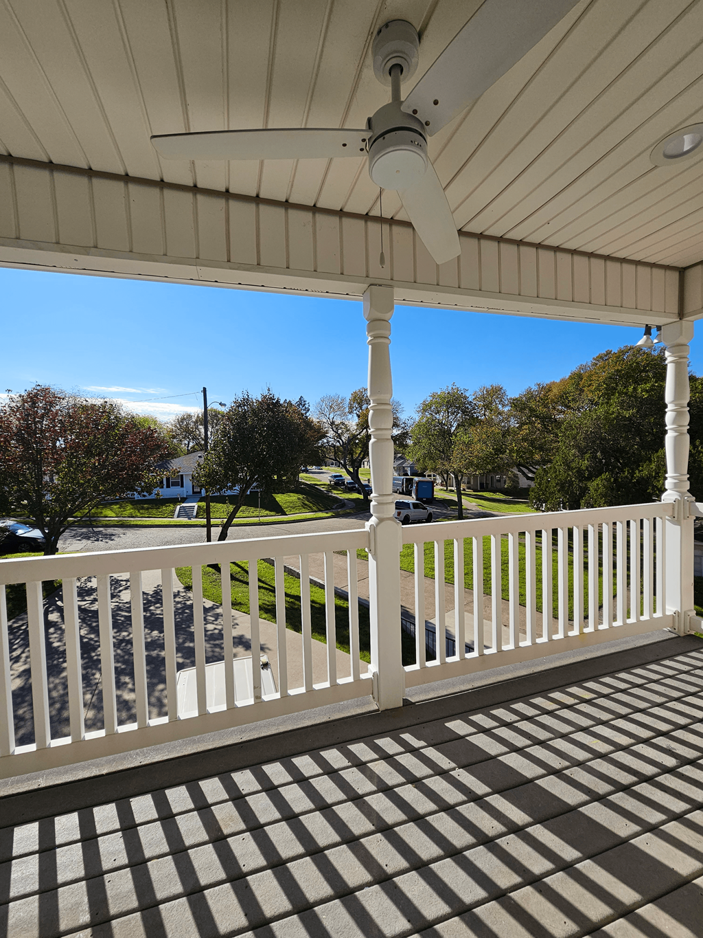 A white porch with a ceiling fan and a view of a street.