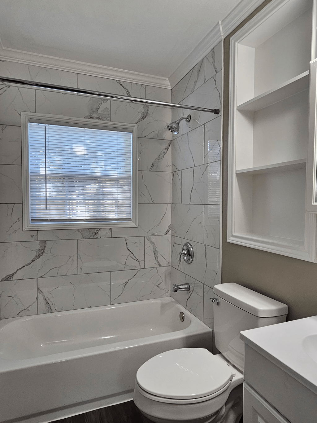 A white toilet sits in a bathroom with a marble tile wall and a window.