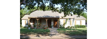 A house with a covered front porch and a tree in front.