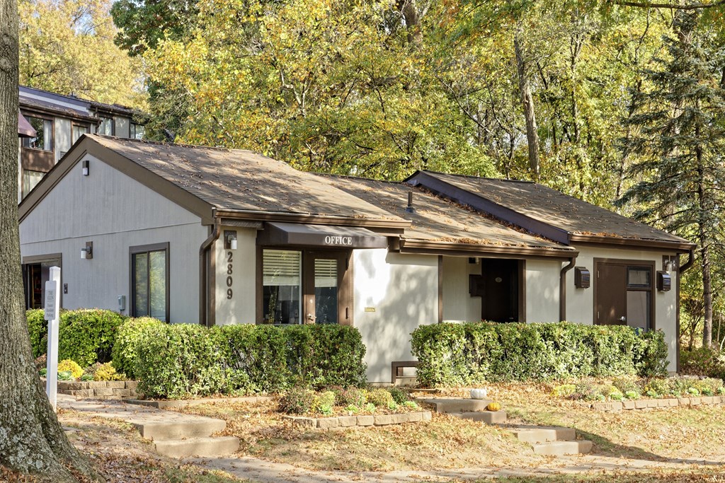 A house with a white facade and a brown roof is surrounded by greenery.