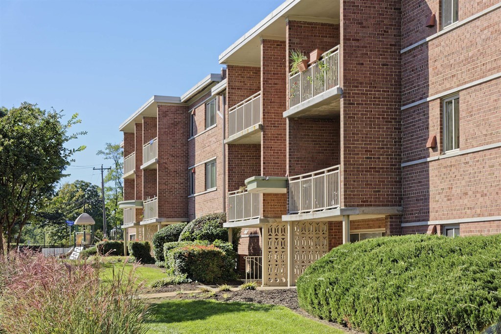 A red brick apartment building with green bushes in front.