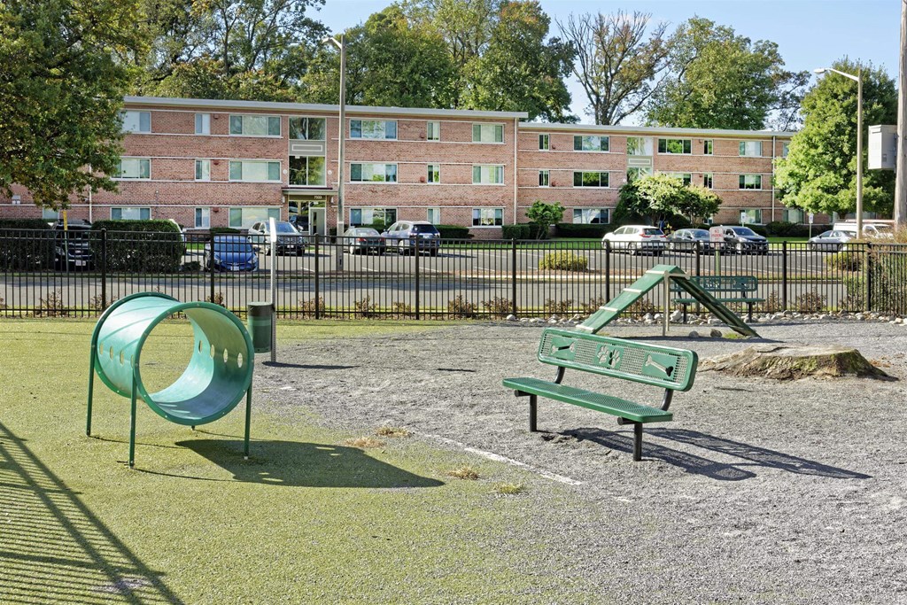 A dog park with a green slide and bench in front of a brick building.