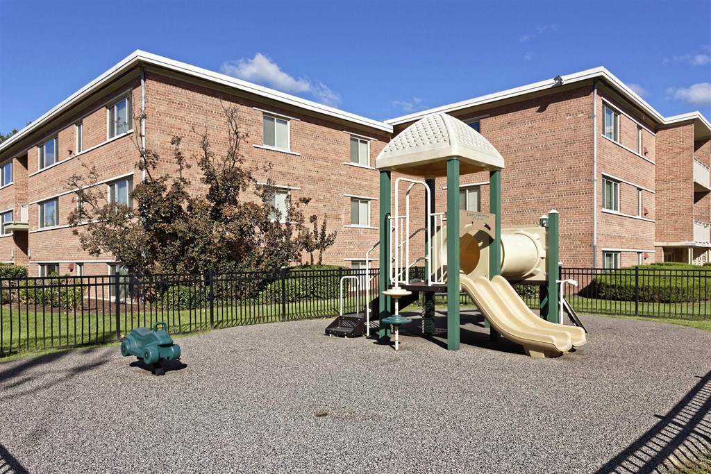 A playground with a slide and a tree in front of a brick building.