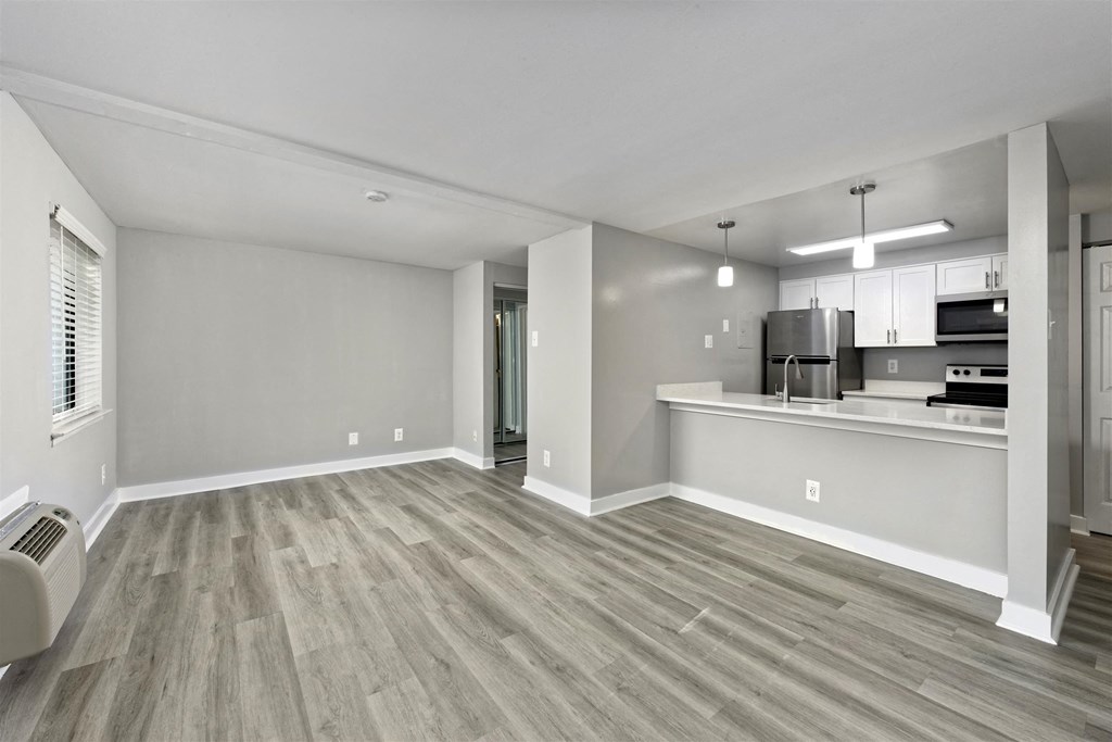A spacious living room with a wood floor and a kitchen area in the background.
