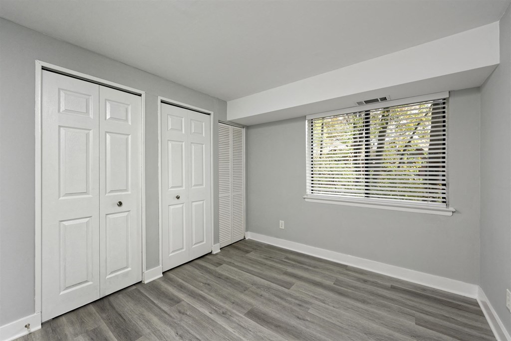 A room with two white doors and a window with blinds.