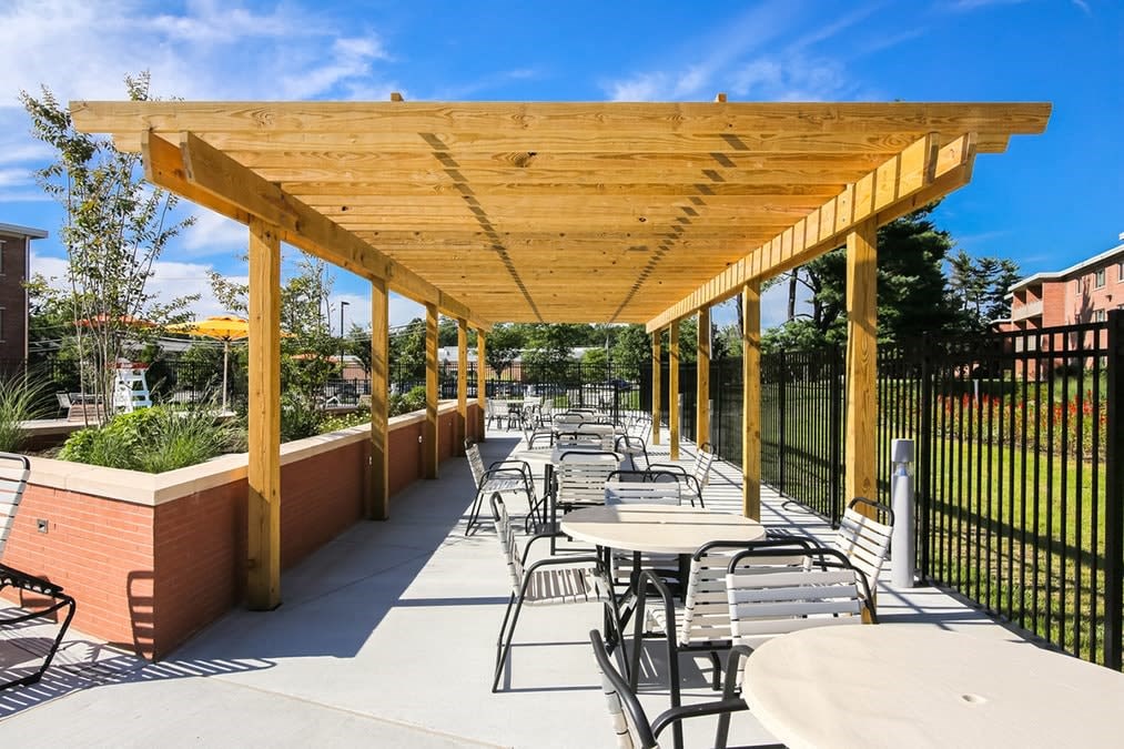 A wooden pergola with tables and chairs is set up on a patio.