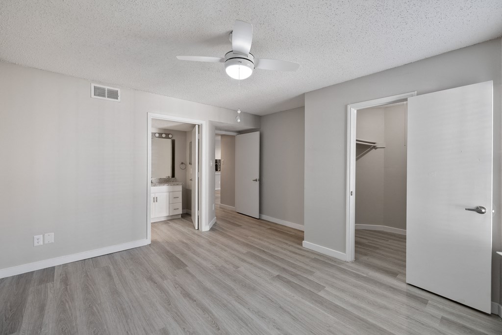 A spacious room with a ceiling fan and light, hardwood floors, and white walls.