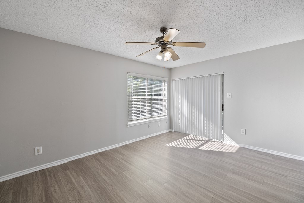 A room with a ceiling fan and light, wooden floors, and a window with blinds.