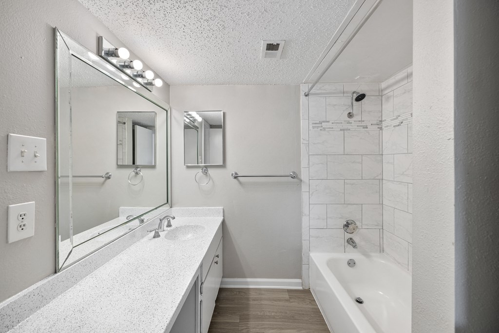 A white bathroom with a sink, mirror, and bathtub.