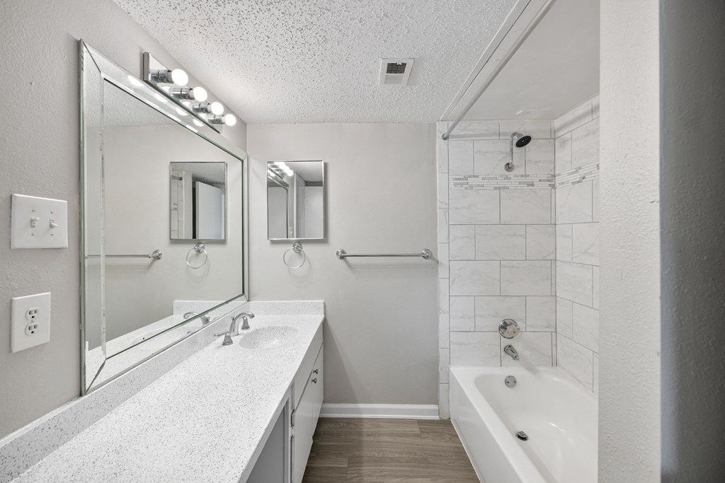 A white bathroom with a sink, mirror, and bathtub.