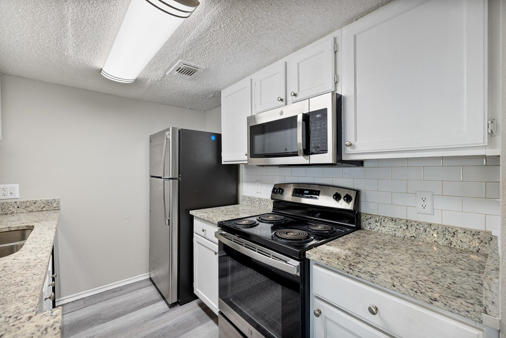 A kitchen with a black refrigerator, stove, and microwave.