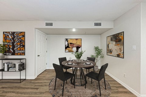 A dining room with a table set for two and a plant on the side table.