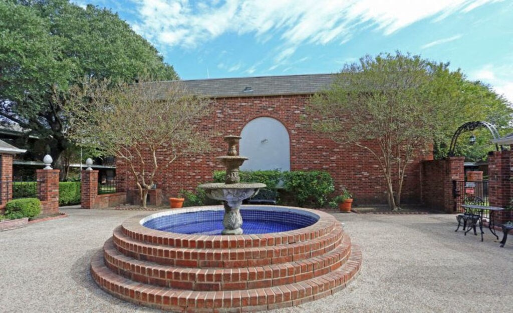 A brick wall with a fountain in the middle of a gravel area.