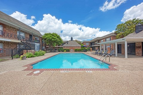 A swimming pool surrounded by a brick building and trees.