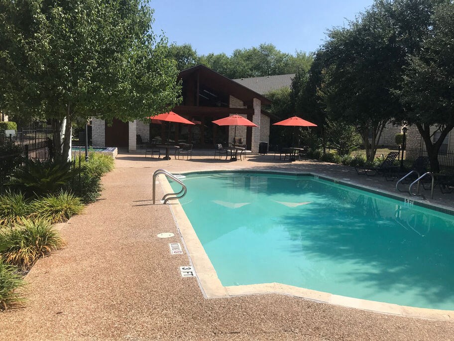 A pool surrounded by trees and umbrellas.