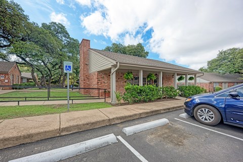 A blue car is parked in a parking space next to a building with a covered porch.