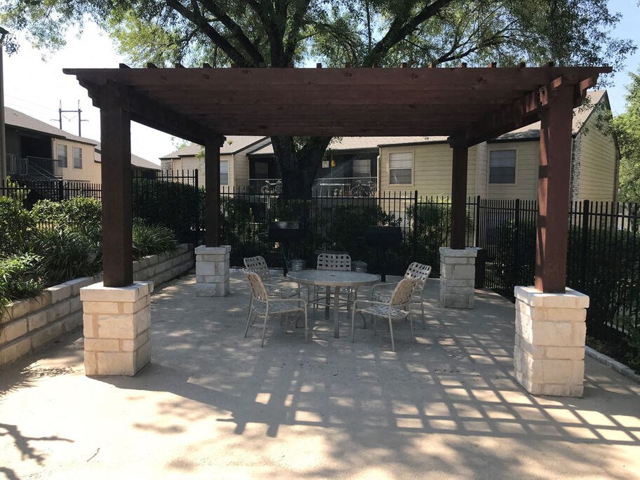 A patio with a table and chairs under a wooden pergola.