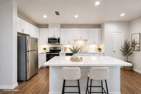 A kitchen with white cabinets and a white island with two chairs.